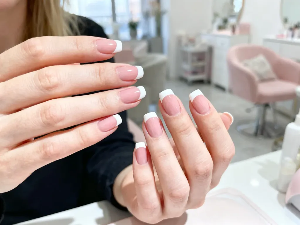 Dłonie z idealnie wykonanym manicure francuskim o białych końcówkach i naturalnej płytce w jasnym, profesjonalnym salonie.