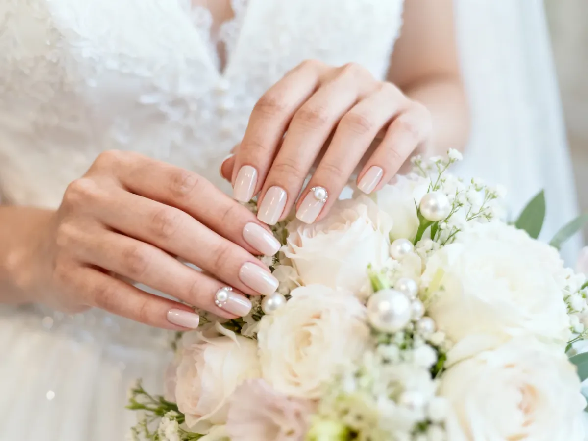 Dłonie panny młodej z eleganckim żelowym manicure przy bukiecie ślubnym